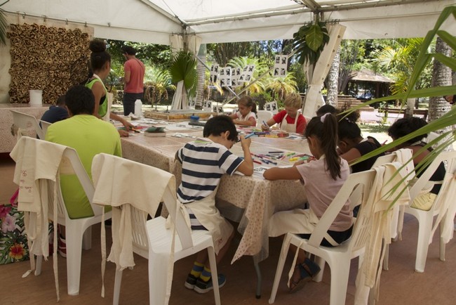 Autour d’une grande table, des enfants apprennent à faire de la sérigraphie avec des feutres dans les mains