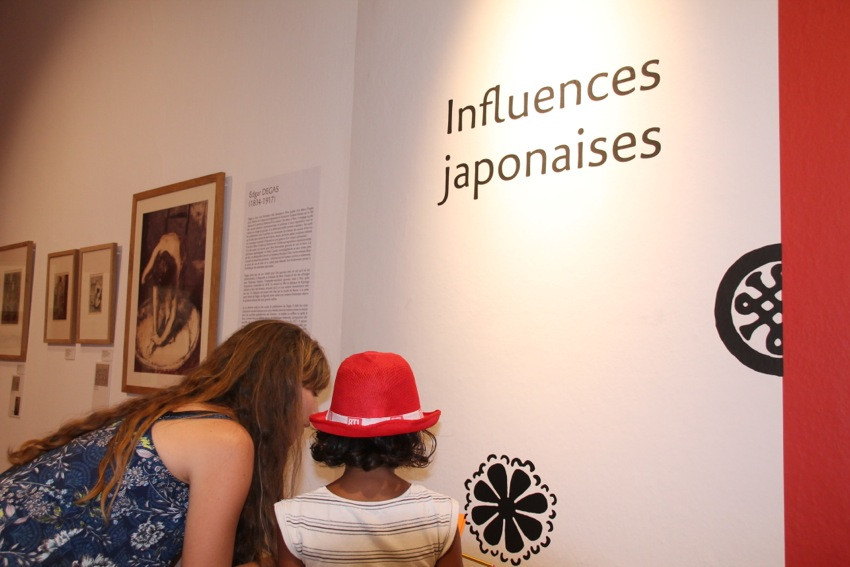 Une animatrice debout à côté d'une petite fille devant un dessin de fleur peint sur le mur du Musée