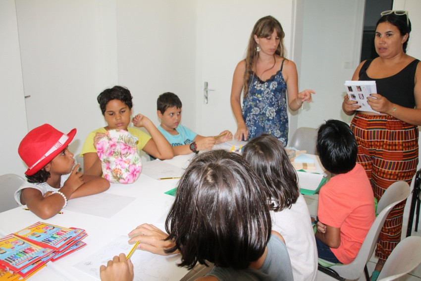 Les enfants assis autour d'une table écoutent les explications des deux animatrices de l'atelier